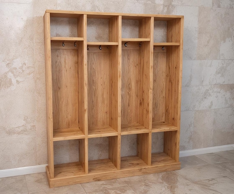 May include: A wooden storage unit with multiple compartments. The unit is made of light-colored wood and features open shelves and hooks for hanging items. The design is simple and functional, suitable for organizing various items.