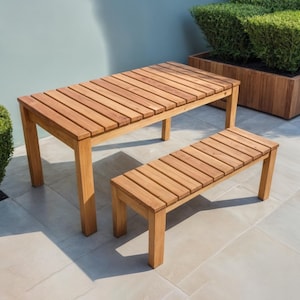 May include: A wooden outdoor dining set with a rectangular table and a bench. The table and bench are made of light brown wood with a slatted design.