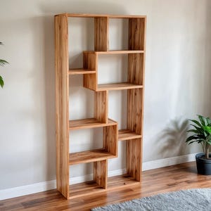 Puede incluir: Una estantería alta de madera con acabado natural. La estantería presenta un diseño único con estantes y compartimentos de diferentes tamaños. La veta de la madera es visible, lo que se suma a la estética natural. La estantería está diseñada para colocarse contra una pared.