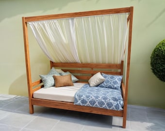 May include: A wooden canopy bed with a white canopy and blue and white patterned bedding. The bed is made of natural wood and has a simple, elegant design.