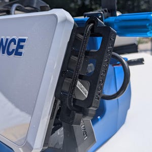 May include: A white and blue Lowrance fish finder with the brand name in blue lettering. The device is mounted on a blue and black bracket. The image is taken outdoors in daylight.