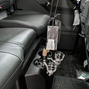 Puede incluir: Vista interior de un vehículo lado a lado negro con dos cañas de pescar y carretes. Las cañas están suspendidas sobre la consola central y los carretes están en los portavasos. Los asientos son de cuero negro.