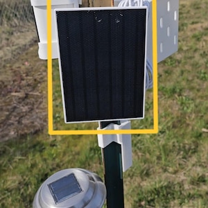 Puede incluir: Un soporte en T blanco para un panel solar Wyze, mostrado montado en un poste de metal negro en un ángulo de 45 grados. El panel solar es negro y rectangular. El texto "T-Clamp Mount for Wyze Solar Panel" está escrito en rojo en la parte superior de la imagen. El texto "Shown here in a 45-degree slot." está escrito en rojo debajo de la primera línea de texto. El texto "Tool Baskets and Solar Light Mounts also visible. Coming soon..." está escrito en rojo en la parte inferior de la imagen.