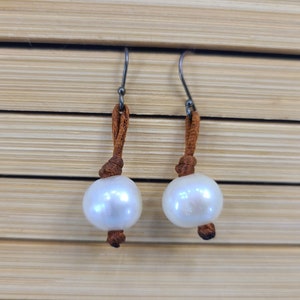 May include: A pair of white pearl earrings with brown leather cord accents.