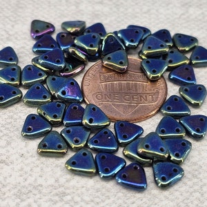 May include: A pile of iridescent blue and green triangle-shaped beads with three holes each. The beads are scattered around a US penny.