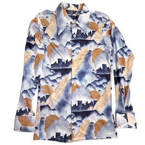 May include: A long-sleeved button-down shirt with a cityscape and abstract design in shades of blue, tan, and white. The shirt features a classic collar and buttoned cuffs. The pattern includes silhouettes of buildings and cloud-like shapes.