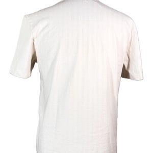 May include: A cream-colored short-sleeved t-shirt displayed on a mannequin. The shirt has a crew neck and a slightly textured appearance. The back of the shirt is visible, showing the simple design.