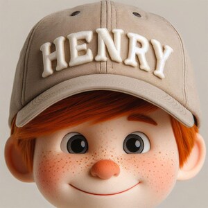 Könnte beinhalten: Nahaufnahme eines Kindergesichts mit roten Haaren und Sommersprossen. Das Kind trägt eine beige Baseballkappe mit dem Namen "HENRY", der in Weiß gestickt ist.