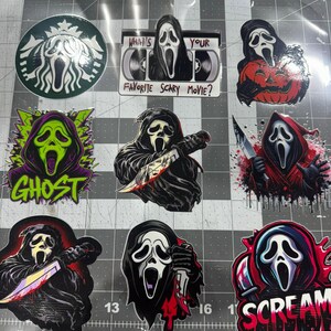 May include: A collection of nine vinyl stickers featuring the Ghostface character from the Scream franchise. Designs include a coffee-inspired logo, a VHS tape with the text "What's Your Favorite Scary Movie?", and various illustrations of the masked figure holding knives, pumpkins, or surrounded by colorful graphic elements and the word "Scream".