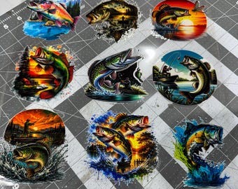 May include: A collection of nine colorful stickers featuring various fish, including bass and trout, depicted in dynamic jumping poses, underwater scenes, and sunset fishing landscapes with vibrant blues, oranges, greens, and yellows on a cutting mat.