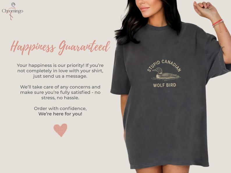 May include: Dark grey t-shirt with the text "STUPID CANADIAN WOLF BIRD" and a graphic of a loon. The shirt also has the text "Happiness Guaranteed" and other text. The shirt is a casual, oversized fit.