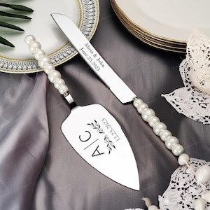Peut inclure: Un ensemble de couteau et de serveur à gâteau en argent avec des manches en perles. Le couteau est gravé avec "Alicia & John June 23, 2023". Le serveur est gravé avec "A/C 1.23.2023" et un motif floral.