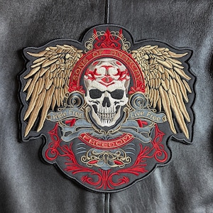 Op de afbeelding: Geborduurde patch met een schedel met vleugels, de tekst "Sons of Anarchy" en de zinnen "Ride Free" en "Live Free". De patch heeft rode, gouden en grijze details op een zwarte achtergrond. Het woord "Freedom" wordt ook weergegeven.