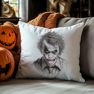 May include: White square pillow featuring a detailed black and white portrait of a character with red lipstick and messy hair. The pillow is on a gray couch with a carved pumpkin and orange blanket in the background. Halloween decor.