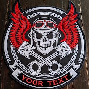 Może przedstawiać: Czarna, haftowana naszywka z czaszką w hełmie i goglach, czerwonymi skrzydłami i skrzyżowanymi tłokami. Projekt otoczony jest łańcuchem i zawiera czerwony tekst "YOUR TEXT".