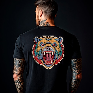 Pode incluir: Camiseta preta com um gráfico colorido e detalhado da cabeça de um urso rugindo. O design do urso inclui tons de amarelo, azul, vermelho e verde. A camiseta é de gola redonda.