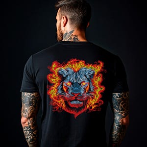 May include: Black t-shirt with a vibrant lion face design on the back. The lion's mane is rendered in fiery red and yellow, contrasting with a blue face and bright yellow eyes. The design is centrally placed on the back of the shirt.