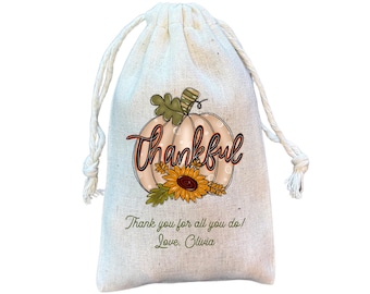 May include: A white drawstring bag with a printed design of a pumpkin with the word "thankful" in orange. The pumpkin has a sunflower and wheat stalks. The text "Thank you for all you do! Love, Olivia" is printed below the pumpkin.