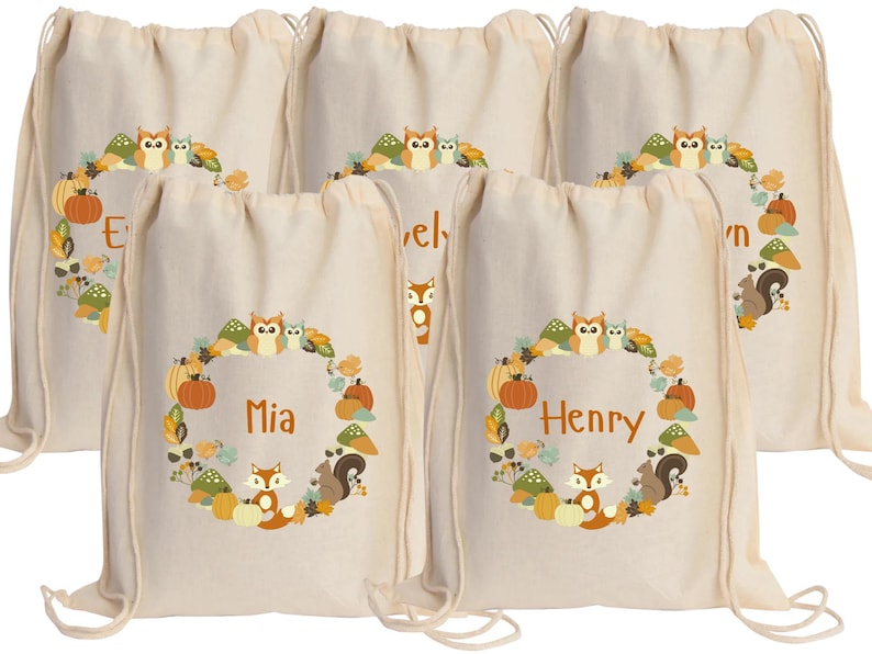 May include: Five white canvas drawstring bags with a woodland animal theme. Each bag has a different name printed on it: Mia, Henry, Evelyn, Owen, and Ethan. The bags feature a circle of woodland animals including owls, foxes, squirrels, and mushrooms.