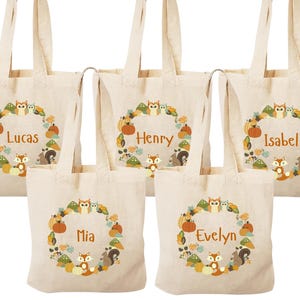 May include: Five beige canvas tote bags with brown handles. Each bag features a circular design with a brown squirrel, a brown owl, and a brown fox. The bags are personalized with the names Lucas, Henry, Isabel, Mia, and Evelyn.