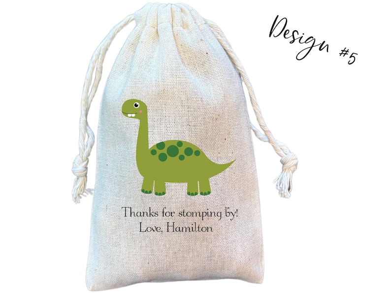 May include: A beige drawstring pouch made of woven fabric featuring a green dinosaur illustration with dark green spots. Below the dinosaur, the text reads: Thanks for stomping by! Love, Hamilton. The top right corner displays the text Design #5.