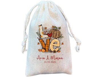 May include: A white burlap drawstring bag with a fall-themed design featuring the word "LOVE" in colorful letters with a pumpkin and leaves. The bag is personalized with the text "Aria & Mason 11-15-2025".