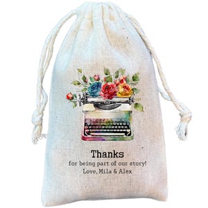 May include: A white cotton drawstring bag with a floral design and a vintage typewriter illustration. The bag has the text "Thanks for being part of our story! Love, Mila & Alex" printed on it.