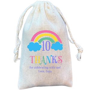 May include: A white cotton drawstring bag with a rainbow and clouds design. The bag has the number 10 and the text "THANKS for celebrating with me! Love, Zaya" printed on it.