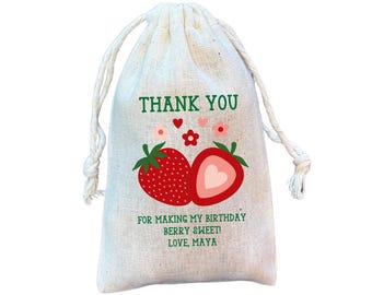May include: A small, beige drawstring bag with a strawberry design and the text "THANK YOU" in green. The bag also says "FOR MAKING MY BIRTHDAY BERRY SWEET! LOVE, MAYA". The bag has a white drawstring closure.