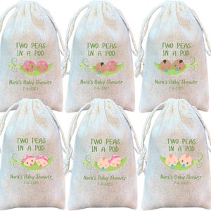 May include: Six white fabric drawstring bags with the text "Two Peas in a Pod" and a cartoon image of two peas in a pod. The bags are decorated with green leaves and the text "Nora's Baby Shower" and the date "7-6-2015".