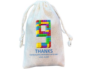 May include: A beige drawstring bag with a colorful number 9 made of toy blocks. The bag has the word "THANKS" and the text "FOR BUILDING MEMORIES WITH ME! LOVE, ELIJAH" printed on it.