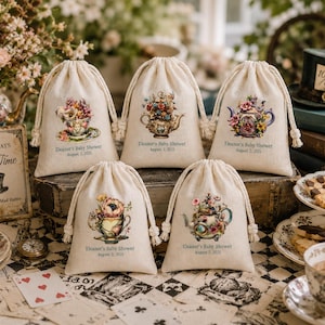 May include: Five off-white drawstring fabric favor bags featuring colorful floral teapot and teacup illustrations. Each bag is printed with the text 'Eleanor's Baby Shower August 2, 2025' in a dark font, with thick cream-colored rope drawstrings.
