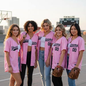 May include: Five people wearing pink baseball jerseys with black pinstripes and the word "Your" or "Teams" on the front. The jerseys have the number "00" on the front. Some people are holding baseball gloves and a bat.