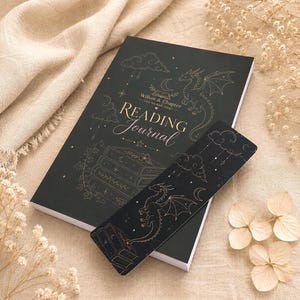 May include: A black reading journal and a matching bookmark, both featuring gold-toned line art of a dragon, clouds, stars, and a stack of books. The journal cover displays the text Willow & Chapter, cosy bookish things, and READING JOURNAL.