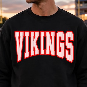 Peut inclure: Un sweat-shirt noir à col rond arborant le mot VIKINGS imprimé dans une grande police de style universitaire arquée. Les lettres sont blanches avec de fines rayures verticales et un contour rouge vif, centrées sur la poitrine du vêtement.