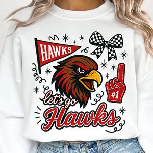 May include: White sweatshirt with a graphic design featuring a red and brown hawk, a pennant that says "Hawks", a foam finger, and the text "Let's go Hawks". The design also includes a checkered bow and stars.