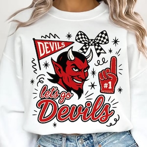 Puede incluir: Sudadera blanca con un diseño rojo y negro. El diseño incluye una cara de diablo, una bandera que dice "Devils", un lazo a cuadros, un dedo de espuma con el número uno y las palabras "Let's Go Devils".