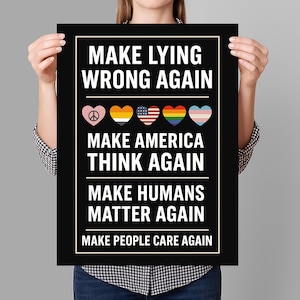 May include: Black and white poster with the text "Make Lying Wrong Again", "Make America Think Again", "Make Humans Matter Again", and "Make People Care Again". The poster also features a row of five hearts with different symbols, including a peace sign, a rainbow, and a transgender flag.