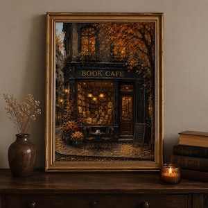 Könnte beinhalten: Ein gerahmter Kunstdruck, der die Fassade eines Buchcafés in der Abenddämmerung zeigt, mit warmer goldener Innenbeleuchtung, büchergefüllten Regalen und herbstlichem Laub. Die Szene umfasst einen kleinen Außentisch mit Stühlen und die Aufschrift BOOK CAFE.