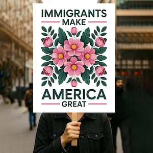 以下が含まれることがあります： 「IMMIGRANTS MAKE AMERICA GREAT」の白い文字が書かれた看板。ピンクの花と緑の葉のフローラルデザインが特徴です。背景はぼやけた街並みです。