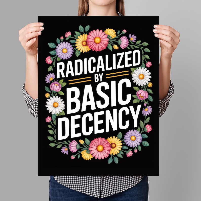 May include: Black poster with the text "RADICALIZED BY BASIC DECENCY" in white, surrounded by a floral wreath of pink, yellow, purple, and white flowers. The poster is held by a person.
