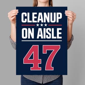 以下が含まれることがあります： 紺色のポスターで、白と赤で「CLEANUP ON AISLE 47」と書かれています。テキストは太字で明確なフォントで配置され、「ON AISLE」の上に赤い線と3つの星があります。「47」の数字は大きく太字の赤色です。
