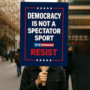 Può includere: Una persona tiene in mano un cartello con la scritta "DEMOCRACY IS NOT A SPECTATOR SPORT" in bianco su sfondo blu navy. Il cartello include anche la parola "RESIST" in rosso, con un bordo rosso e bianco.