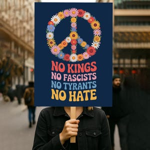 May include: A dark blue sign with a peace symbol made of colorful flowers. The sign reads "NO KINGS, NO FASCISTS, NO TYRANTS, NO HATE" in a retro font. The sign is held up in front of a person.