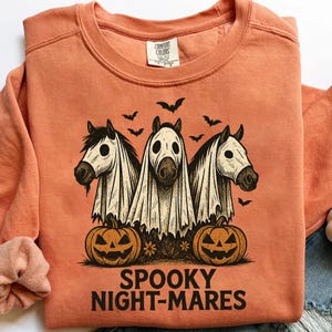 May include: Orange sweatshirt with a Halloween-themed graphic. The design features three white horses wearing ghost costumes, jack-o'-lanterns, and bats. The text "SPOOKY NIGHT-MARES" is printed below the graphic.