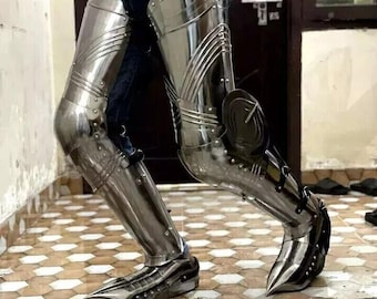 May include: A pair of silver metal leg armor with a pointed toe design. The armor is worn over jeans and covers the legs from the thigh to the foot.