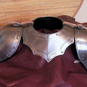 Può includere: Un set di armature per spalle in metallo color argento con cinturini in pelle. L'armatura è composta da due piastre per le spalle e una protezione per il collo.