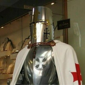 May include: A silver knight's armor with a white cape and a red cross. The knight is wearing a helmet with a gold cross on the front.
