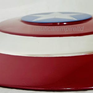 May include: A red, white and blue Captain America shield replica. The shield is made of metal and has a raised star in the centre.
