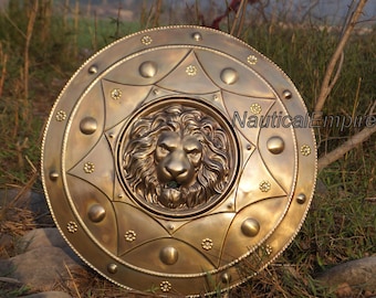 Puede incluir: Un escudo grande, redondo y de color dorado con una cabeza de león en relieve en el centro. El escudo tiene un patrón decorativo de círculos y estrellas alrededor de la cabeza del león.